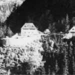 Schwarz-Weiß-Foto von zwei Gebäuden, umgeben von dichtem Wald, auf einem Berg oder Hügel gelegen.