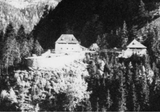 Schwarz-Weiß-Foto von zwei Gebäuden, umgeben von dichtem Wald, auf einem Berg oder Hügel gelegen.