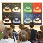 Eine Gruppe von Kindern steht vor zwei bunten Pop-Art-Gemälden von Autos, die nebeneinander in einer Galerie ausgestellt sind.