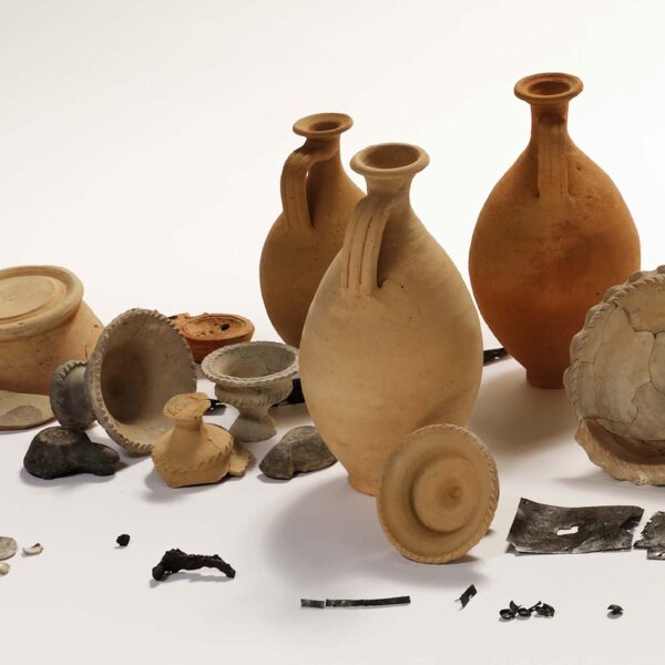 Eine Sammlung von antiken Keramikgefäßen, Keramikscherben, Münzen, Metallfragmenten und kleinen Artefakten auf weißem Hintergrund.