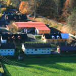 Luftaufnahme eines kleinen Museumskomplexes mit mehreren Gebäuden, umgeben von Bäumen und Grasflächen, am Rande eines Waldes gelegen.