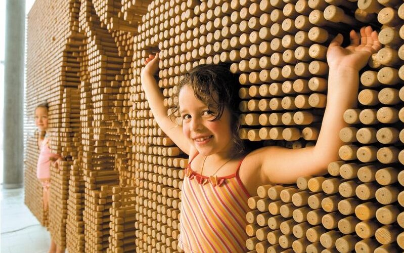 Zwei junge Mädchen spielen mit einer großen interaktiven Wand aus Holzpflöcken und drücken ihre Körper in die Pflöcke, um Abdrücke ihrer Umrisse zu erzeugen.