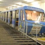 Ein blauer Standseilbahnwagen mit der Aufschrift "Großglockner" steht an einer steilen Steigung in einem Betontunnel, der auf beiden Seiten mit Geländern versehen ist.