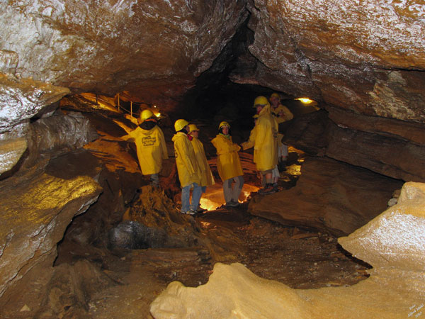 Mehrere Personen mit gelben Regenmänteln und Helmen stehen in einer Felshöhle, die von künstlichen Lichtern beleuchtet wird.
