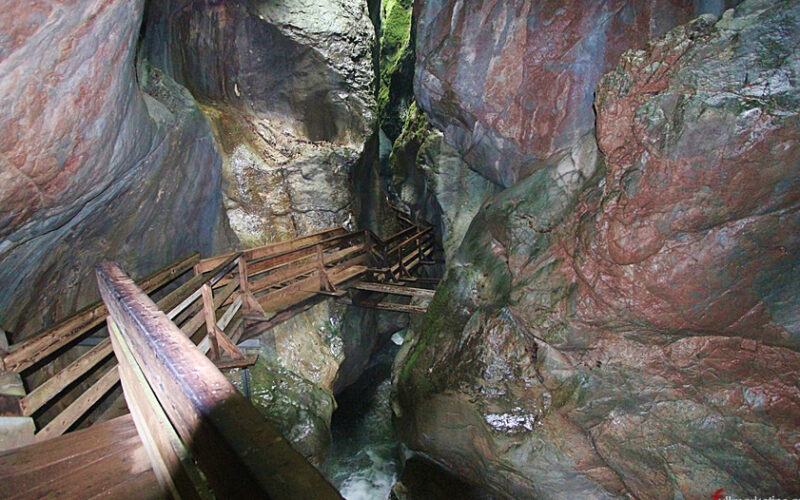 Holzstege führen durch eine enge, felsige Schlucht mit steilen Steinwänden und spärlichem Grün darüber.