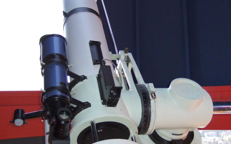 Ein großes weißes Teleskop, das in einer Observatoriumskuppel montiert und auf einen offenen Teil der Kuppel ausgerichtet ist.