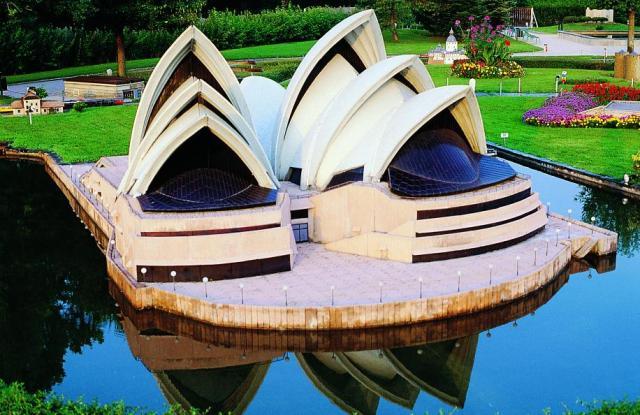 Ein verkleinertes Modell des Opernhauses von Sydney steht neben einem Teich, umgeben von grünem Gras und bunten Blumenbeeten.