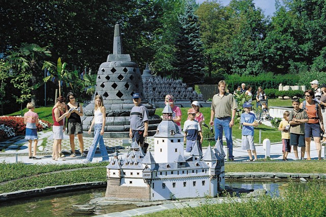 Eine Gruppe von Menschen, darunter Kinder und Erwachsene, steht im Freien und betrachtet Miniaturnachbildungen berühmter Wahrzeichen inmitten von Grünflächen.