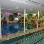 Hallenbad mit bunten Liegestühlen, modernem Dekor und farbigen Lichtern, die sich auf dem Wasser spiegeln.