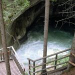 Von einer hölzernen Aussichtsplattform aus überblickt man ein von Felsen und Bäumen umgebenes Wasserbecken in einem bewaldeten Gebiet.