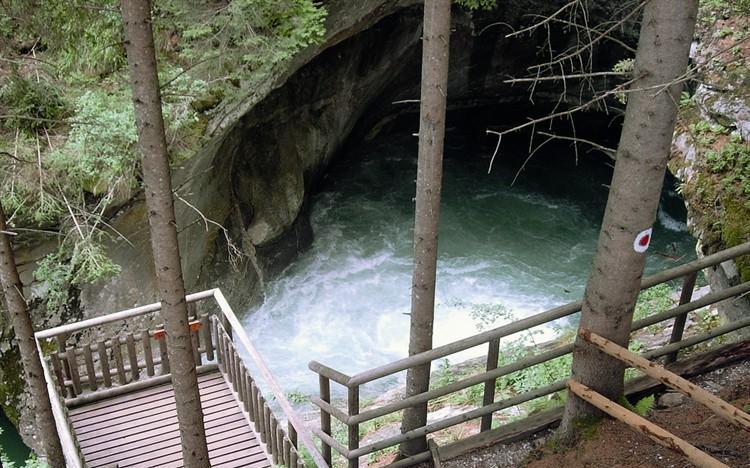 Von einer hölzernen Aussichtsplattform aus überblickt man ein von Felsen und Bäumen umgebenes Wasserbecken in einem bewaldeten Gebiet.