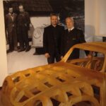 Zwei Männer stehen vor einem großen alten Foto und neben einem hölzernen Autorahmen, der in einem Museum ausgestellt ist.