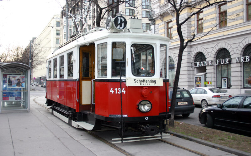 Rot-weiße Oldtimer-Straßenbahn mit der Nummer 4134 hält an einer Straßenbahnhaltestelle in einer von Autos und historischen Gebäuden gesäumten Straße.
