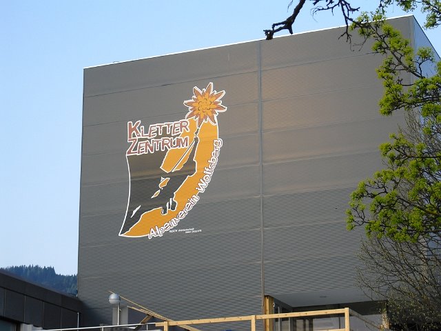 Ein graues Gebäude mit einem großen Schild mit der Aufschrift "Kletterzentrum" und der Abbildung eines Kletterers, eines Berges und einer Edelweißblume.