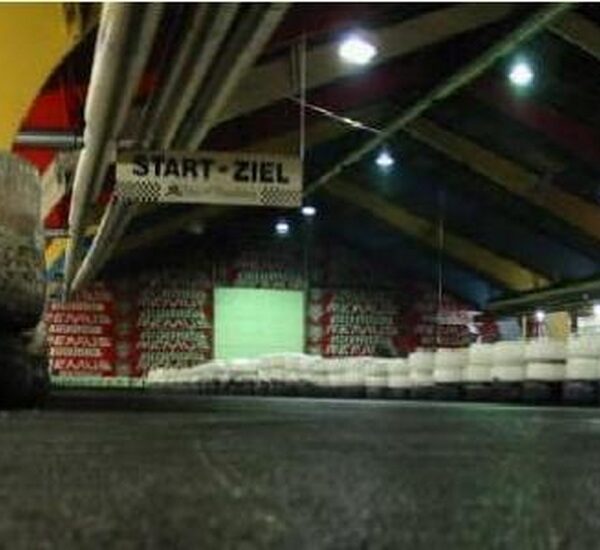 Indoor-Gokartbahn mit Reifenabsperrungen, einem START-ZIEL (Start-Ziel)-Banner über dem Kopf und bunten Balken an der Decke.