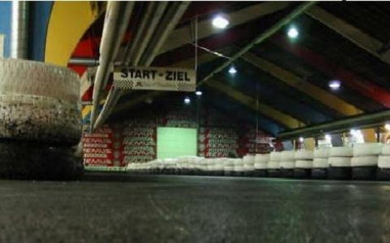 Indoor-Gokartbahn mit Reifenabsperrungen, einem START-ZIEL (Start-Ziel)-Banner über dem Kopf und bunten Balken an der Decke.