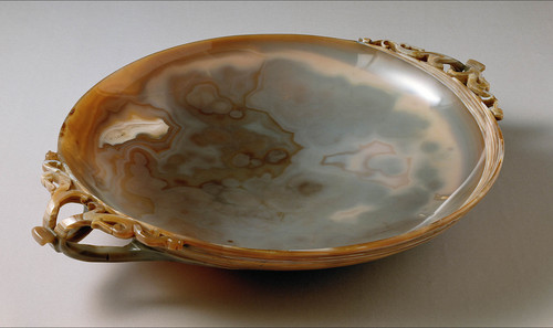 Eine flache, runde Schale aus Achat mit kunstvoll geschnitzten Henkeln auf jeder Seite, die natürliche Muster in Braun- und Grautönen aufweisen.