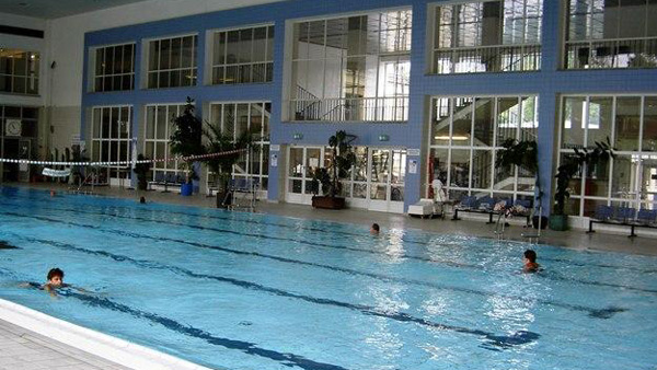 Hallenbad mit Schwimmbahnen, mehreren Schwimmern und einer Kulisse aus großen Fenstern und Sitzbereichen.