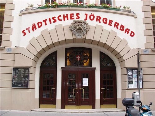 Eingang des Städtischen Jörgerbads mit Rundbogenportal, Glasscheiben und roter Beschilderung über der Tür.