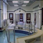 Innen-Spa-Bereich mit einem kleinen runden Pool, weißen Liegestühlen, gefliesten Wänden, Spiegeln und Waschbecken an der Rückwand.