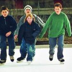 Vier Kinder in Winterjacken und Pullovern, die tagsüber im Freien Schlittschuh laufen.