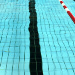 Schwimmbadwasser mit Bahnmarkierungen auf dem Boden und einem rot-weißen Bahntrenner, der auf der rechten Seite schwimmt.