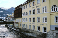 Ein gelbes Gebäude mit der Aufschrift "Kranken-Gebäu" und "Sanatorium Montafon" steht neben einem felsigen Fluss, im Hintergrund sind Berge zu sehen.