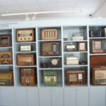Eine Ausstellung von alten Radios verschiedener Größen und Stile, die in einem Museum oder einer Ausstellung in Regalen angeordnet sind.