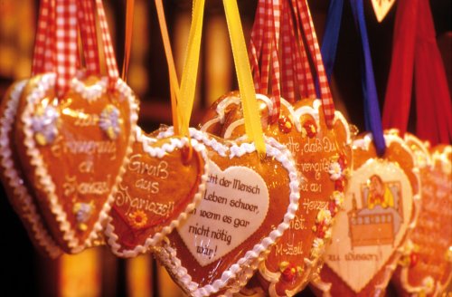 Herzförmige Lebkuchen mit dekorativem Zuckerguss und deutscher Schrift, die an bunten Bändern an einem Marktstand hängen.