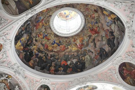 Verziertes Kuppelgewölbe mit zentralem Oberlicht, das ein detailliertes Fresko mit zahlreichen Figuren in leuchtenden Farben zeigt, umgeben von dekorativem weißem Stuck.