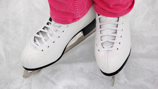 Eine Person mit weißen Schlittschuhen und rosa Hosen steht auf einer Eisbahn.