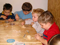 Vier kleine Kinder sitzen an einem Holztisch und formen mit ihren Händen und kleinen Werkzeugen Teig.