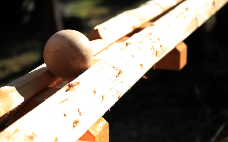 Eine Holzkugel wird auf zwei rauen, unbearbeiteten Holzbrettern im Freien in hellem Sonnenlicht platziert.