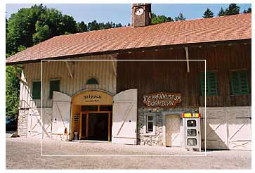 Ein rustikales Holzgebäude mit einem Uhrenturm mit der Aufschrift "Rappenlochmuseum Dornbirn" und einem Verkaufsautomaten in der Nähe des Eingangs.