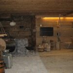 Die rustikale Holzküche ist mit altmodischen Kochgeräten, Fässern, einem Steinofen und Milchkannen ausgestattet und verfügt über schummriges Licht und Holzmöbel.