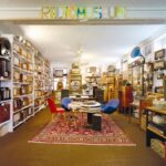 Ein Raum voller alter Radios und Audiogeräte in Regalen, mit einem runden Tisch und bunten Stühlen auf einem roten Teppich in der Mitte; darüber ein Schild mit der Aufschrift "RADIO MUSEUM".