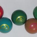 Fünf bunte Gummibälle mit goldenen Etiketten sind auf einer hellen Fläche angeordnet.