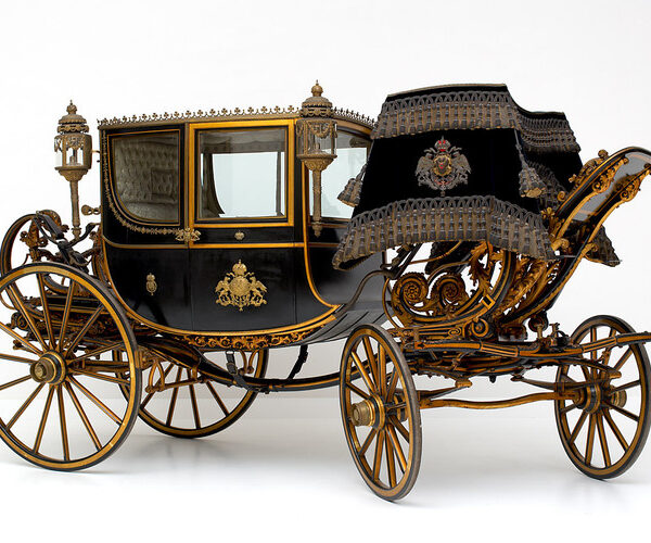 Eine schwarz-goldene verschnörkelte Pferdekutsche mit aufwändigen Details, großen Speichenrädern und dekorativen Laternen vor einem schlichten weißen Hintergrund.