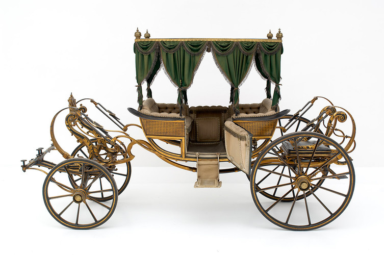 Elegante Vintage-Pferdekutsche mit grün drapiertem Vordach, getufteten Sitzen und detaillierten goldenen Akzenten, dargestellt vor einem schlichten weißen Hintergrund.