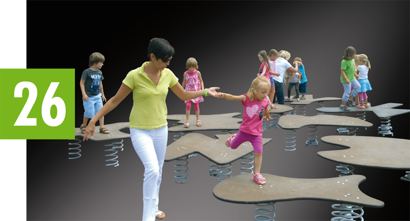 Ein Erwachsener hilft einem Kind, auf einer gefederten Spielplatzplattform das Gleichgewicht zu halten, während andere Kinder im Hintergrund spielen.