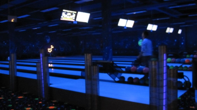 Eine Person bereitet sich darauf vor, in einer schwach beleuchteten Bowlingbahn mit leuchtenden Bahnen und Bildschirmen über der Decke zu bowlen.