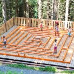 Vier Kinder und ein Erwachsener laufen durch ein kleines, von einem Zaun umgebenes Holzlabyrinth in einem Waldgebiet.