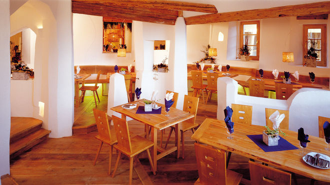 Ein modernes Restaurant mit Holztischen und -stühlen, weißen Wänden, freiliegenden Holzbalken und säuberlich gefalteten Servietten auf jedem Tisch.