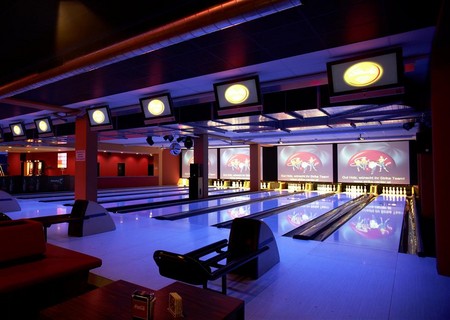 Moderne Bowlingbahn mit mehreren Bahnen, elektronischen Anzeigetafeln über dem Kopf, Loungesitzplätzen und bunter Beleuchtung, die eine lebendige Atmosphäre schafft.