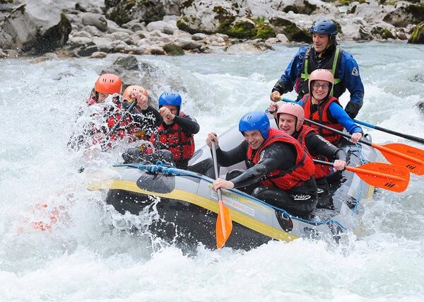 Eine Gruppe von sechs Personen, die Helme und Schwimmwesten tragen, paddelt auf einem Fluss durch plätschernde Wellen.