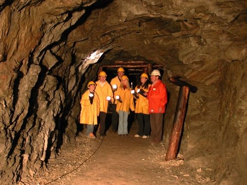 Eine Gruppe von Personen mit Schutzhelmen und gelben Jacken steht in einem schwach beleuchteten Felstunnel und hält Taschenlampen in der Hand.