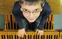 Ein Junge mit Brille blickt in die Kamera, während er ein Tasteninstrument spielt.