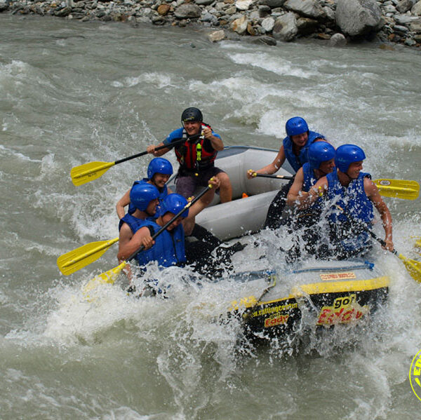 Sechs Personen mit blauen Helmen und Schwimmwesten beim Wildwasser-Rafting auf einem rauen Fluss, die durch das spritzende Wasser paddeln. In der unteren rechten Ecke ist ein Logo für "Sport Rafting" zu sehen.