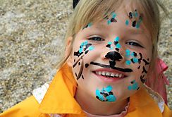 Lächelndes Kind mit gelber Jacke und tierähnlicher Gesichtsbemalung mit blauen und schwarzen Flecken und Schnurrhaaren.