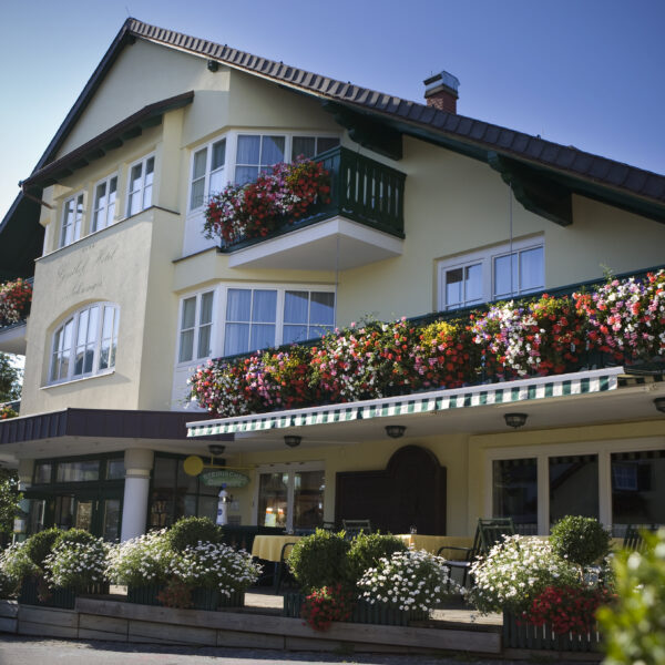 Ein dreistöckiges Haus mit Balkonen und Fenstern, die mit bunten Blumenkästen und grünen Geländern geschmückt sind, unter einem klaren blauen Himmel.